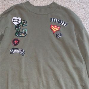 A green long sleeve shirt with sewed in patches